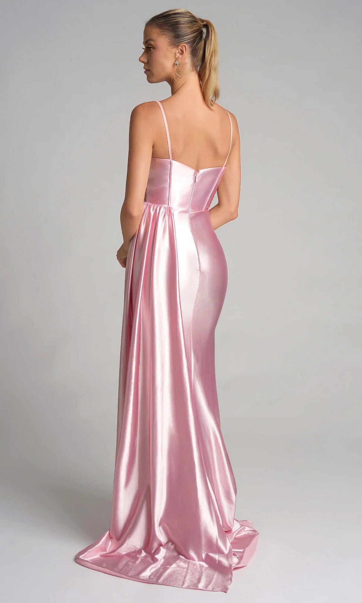 Woman wearing the Portia and Scarlett PS26270 long prom dress in shiny light pink satin with thin straps and a sheer corset bodice, standing with her back to the camera, hair in a ponytail, against a light gray background.